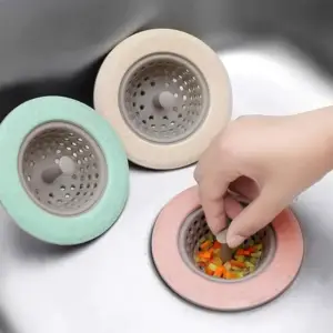 Drei runde Abflusssiebe mit farbigem Rand und grauem Einsatz in Mint, Beige und Rosa in einer Spüle