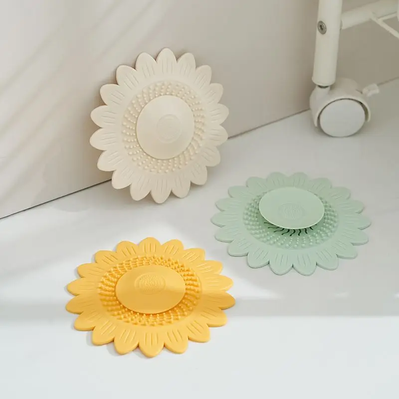 Drei Abflussabdeckungen in Sonnenblumenform in Cremeweiß, Mintgrün und Gelb liegen auf einem weißen Untergrund