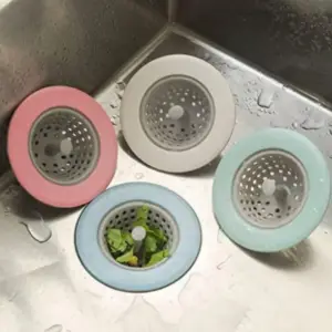 Vier runde Abflusssiebe in Rosa, Beige, Mintgrün und Blau mit grauem Lochkorb liegen in einer Spüle