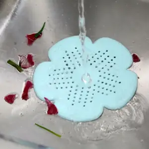 Mintgrünes blütenförmiges Silikon-Abflusssieb in einer Spüle, Wasser fließt hindurch, Blütenblätter liegen daneben