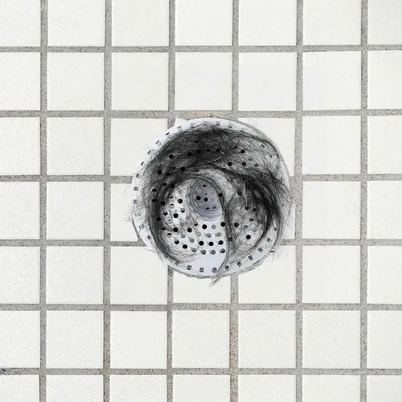Weißes Abflusssieb mit Lochmuster liegt im gefliesten Boden und fängt dunkle Haare auf